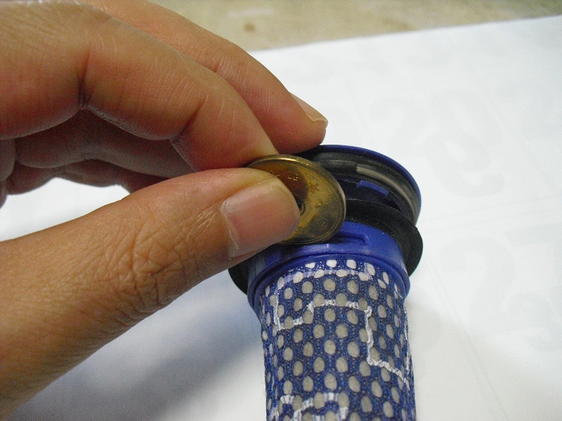 dyson ダイソンのフィルターのフック部分にコインを押し込んで、フックを外している写真